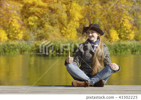 Girl in a hat and coat sitting on the pier Girl in a hat and coat sitting on the pier 43302225