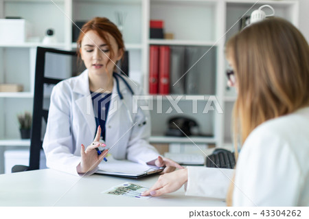 A beautiful young girl in a white robe is sitting at the desk in the office and communicating with A beautiful young girl in a white robe is sitting at the desk in the office and communicating with 43304262