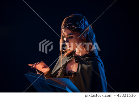 Side view of mystic female beatiful elf reading magical book in darkness. 43321530