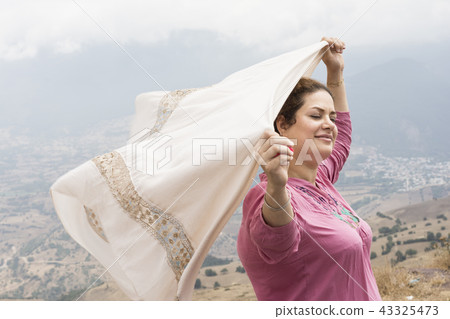 Woman with closed eyes holding a scarf in hands Woman with closed eyes holding a scarf in hands 43325473