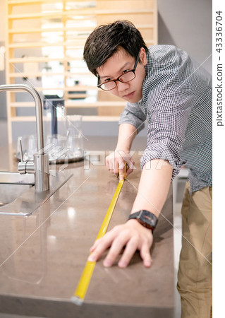 Asian man using tape measure on kitchen counter 43336704
