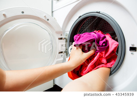 Photo of woman hands folding pink things in washing machine with open door 43345939