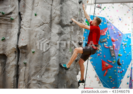 Photo from side of sports man in red T-shirt training on climbing wall Photo from side of sports man in red T-shirt training on climbing wall 43346076