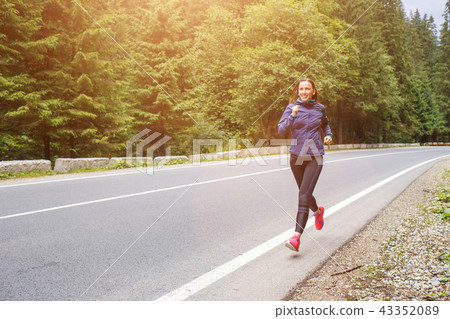 Young smiling woman jogging on mountain road. 43352089