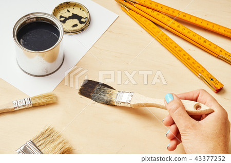 hand is holding a brush with paint and painting a wooden table hand is holding a brush with paint and painting a wooden table 43377252
