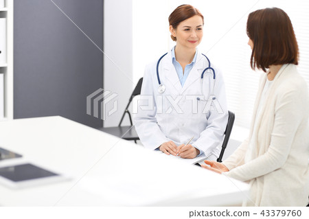 Happy doctor and patient discussing something while sitting at the chairs at hospital. Physician Happy doctor and patient discussing something while sitting at the chairs at hospital. Physician 43379760