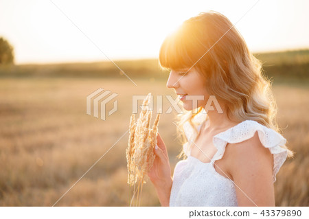 Girl in white dress with spikelets. Woman in field, place for text. Spike and girl in field. Late 43379890