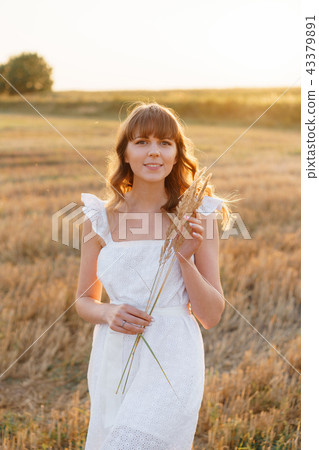 Girl in white dress with spikelets. Woman in field, place for text. Spike and girl in field. Late 43379891