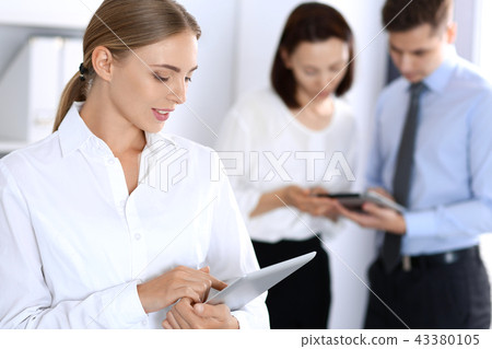 Beautiful blonde business woman using tablet or touch-pad on background of colleagues in office Beautiful blonde business woman using tablet or touch-pad on background of colleagues in office 43380105