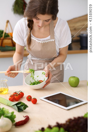 Young brunette woman cooking in kitchen. Housewife holding wooden spoon in her hand. Food and health 43389059