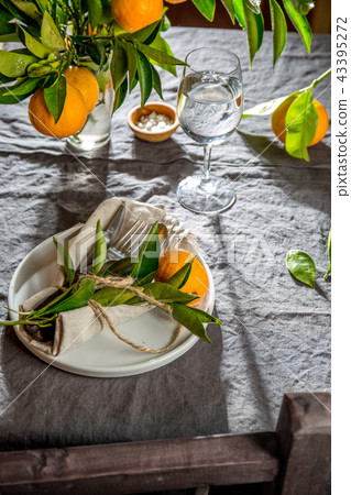 Table setting with white plate, cutlery, linen napkin and orange tree branch decoration on gray 43395272