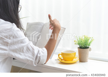 Asian woman reading book beside coffee shop window Asian woman reading book beside coffee shop window 43400940