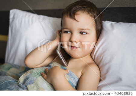 happy small boy talking mobile phone lying on the bed in morning happy small boy talking mobile phone lying on the bed in morning 43408925