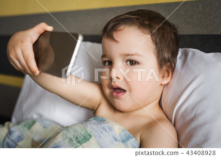 smart cute boy taking photo on phone lying on the bed in morning smart cute boy taking photo on phone lying on the bed in morning 43408928