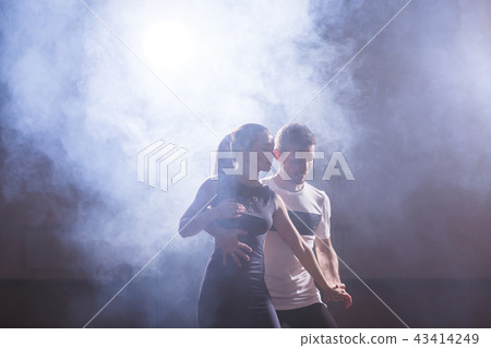 Skillful dancers performing in the dark room under the concert light and smoke. Sensual couple Skillful dancers performing in the dark room under the concert light and smoke. Sensual couple 43414249