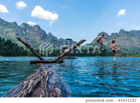 Two Teenage Kids Jumping in the lake with mountains and rain forest in the background during a sunny 43415197