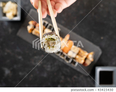 Chopstick with a sushi in focus and a mix of sushi on dark stone Chopstick with a sushi in focus and a mix of sushi on dark stone 43415430