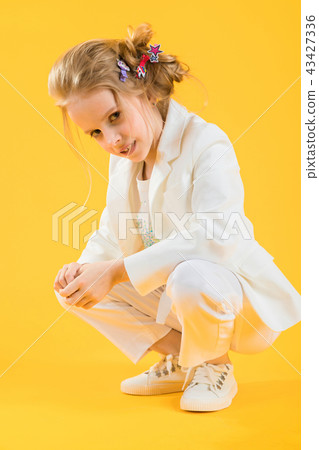 A teenage girl in white clothes is squatting on a yellow background. 43427336