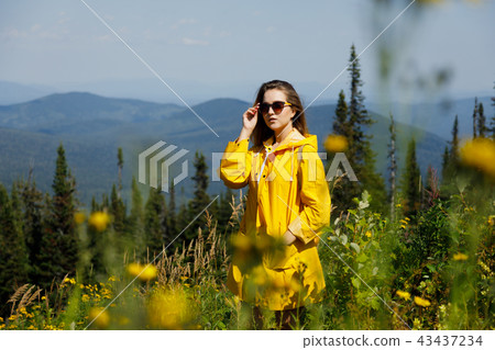 stylish hipster woman in yellow raincoat traveler with backpack on top of mountains, travel concept 43437234