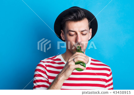 Portrait of a young man in a studio drinking from a bottle on a blue background. Portrait of a young man in a studio drinking from a bottle on a blue background. 43438915