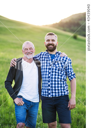 A portrait of an adult hipster son with senior father in nature at sunset. 43439040