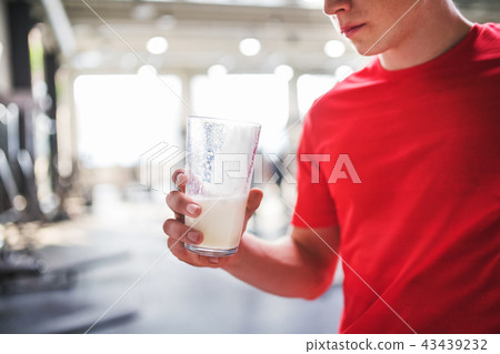 Young man in gym holding a glass of protein drink. Copy space. 43439232