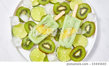 Yoghurt ice cream lolly with a piece of peach in a plate with fresh slices of lime, kiwi and ice 43445693