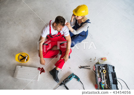 A woman with smartphone helping man worker after an accident at the construction site. A woman with smartphone helping man worker after an accident at the construction site. 43454056