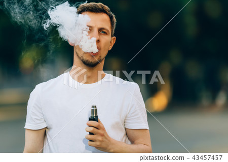 Modern young man with a beard fun Vaporizers Outdoor. Male in white t-shirt vape ecig. dark 43457457
