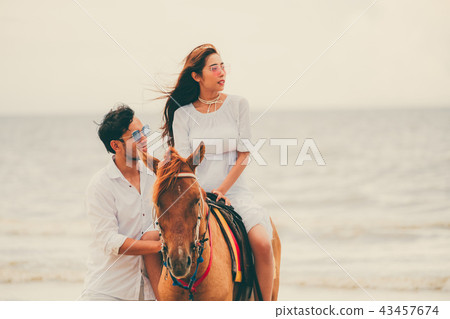 Young couple goes horse riding on tropical beach. 43457674