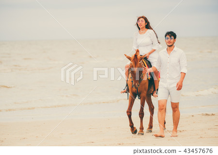 Young couple goes horse riding on tropical beach. 43457676