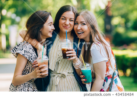 Summer lifestyle portrait multiracial women enjoy nice day, holding glasses of milkshakes. Happy 43458484