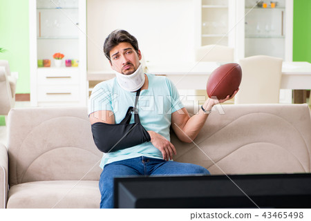 Man with neck and arm injury watching american football on tv Man with neck and arm injury watching american football on tv 43465498