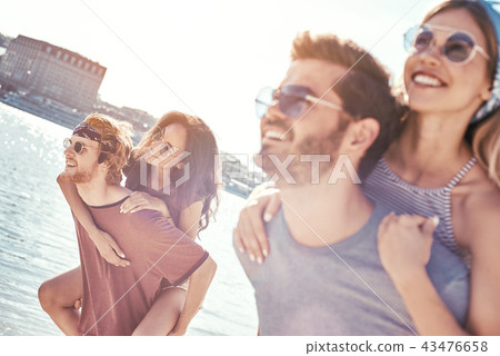 Outdoors photo of happy boyfriends piggybacking their girlfriends at sunset on beach Outdoors photo of happy boyfriends piggybacking their girlfriends at sunset on beach 43476658