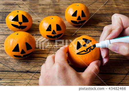 Hands draw a face on a tangerine on Halloween Hands draw a face on a tangerine on Halloween 43482466