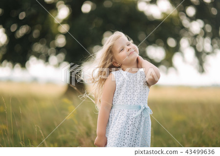 Little girl in sky blue dress stand in field in front of big tree 43499636
