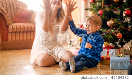 Portrait of happy laughing toddler boy throwing colorful confetti with mother on Christmas morning 43504382