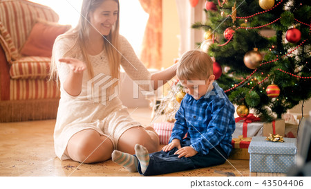 Portrait of happy laughing mother with toddler boy sitting next to Christmas tree at morning Portrait of happy laughing mother with toddler boy sitting next to Christmas tree at morning 43504406