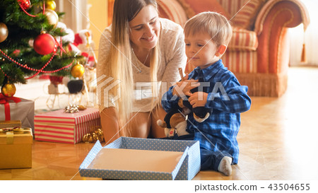 Portrait of happy little boy sitting under Christmas tree with open gift box Portrait of happy little boy sitting under Christmas tree with open gift box 43504655