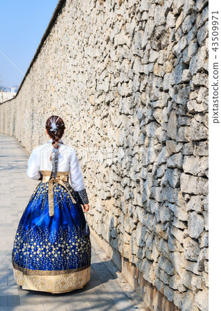 A woman walking in a hanbok and standing beside a high stone wall A woman walking in a hanbok and standing beside a high stone wall 43509971