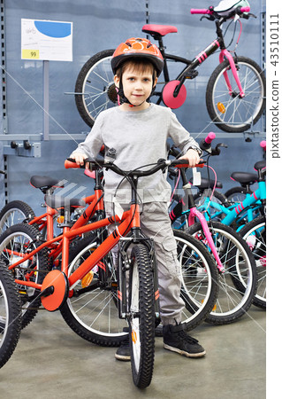 Boy in helmet chooses with bicycle in sport shop Boy in helmet chooses with bicycle in sport shop 43510111