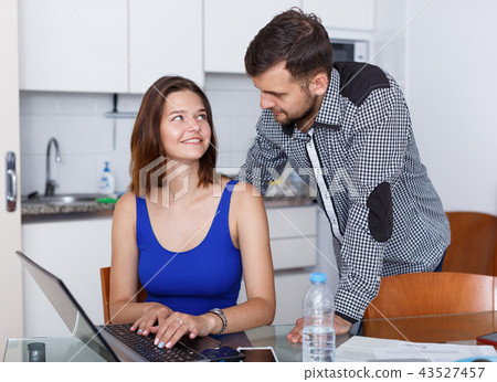 Young woman looking at laptop and man standing at home Young woman looking at laptop and man standing at home 43527457