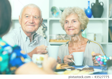 Smiling elderly spouses enjoying tea with girl Smiling elderly spouses enjoying tea with girl 43527775