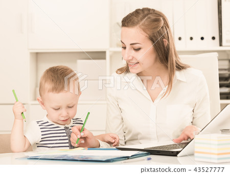 Woman 22-27 years old is working on laptop while child painting on papers Woman 22-27 years old is working on laptop while child painting on papers 43527777