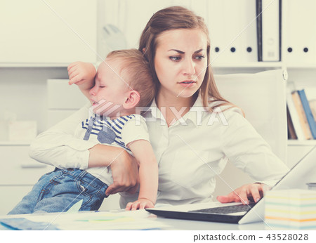 Female is working with a naughty kid in her arms behind a laptop Female is working with a naughty kid in her arms behind a laptop 43528028