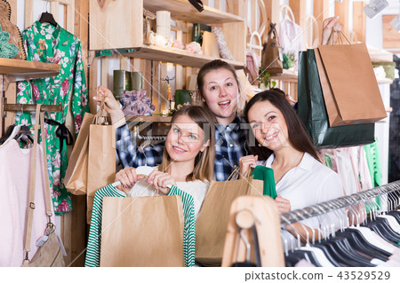 Women friends carrying paper bags with purchases and clothes in shop Women friends carrying paper bags with purchases and clothes in shop 43529529