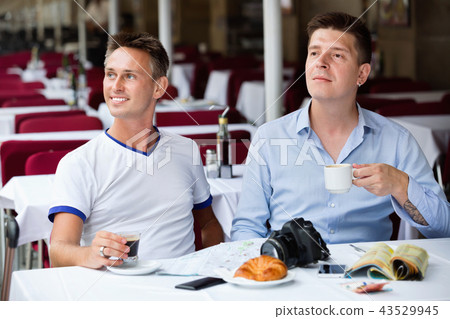 Couple of male tourists talking and drinking coffee Couple of male tourists talking and drinking coffee 43529945