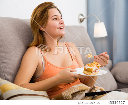 smiling female eating sweet cake on sofa 43530317