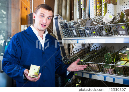 man seller wearing uniform having metal furniture in hands in store man seller wearing uniform having metal furniture in hands in store 43530807