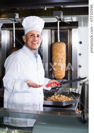 man chef wearing uniform cutting meat for kebab on kitchen in fast food restaurant man chef wearing uniform cutting meat for kebab on kitchen in fast food restaurant 43530996